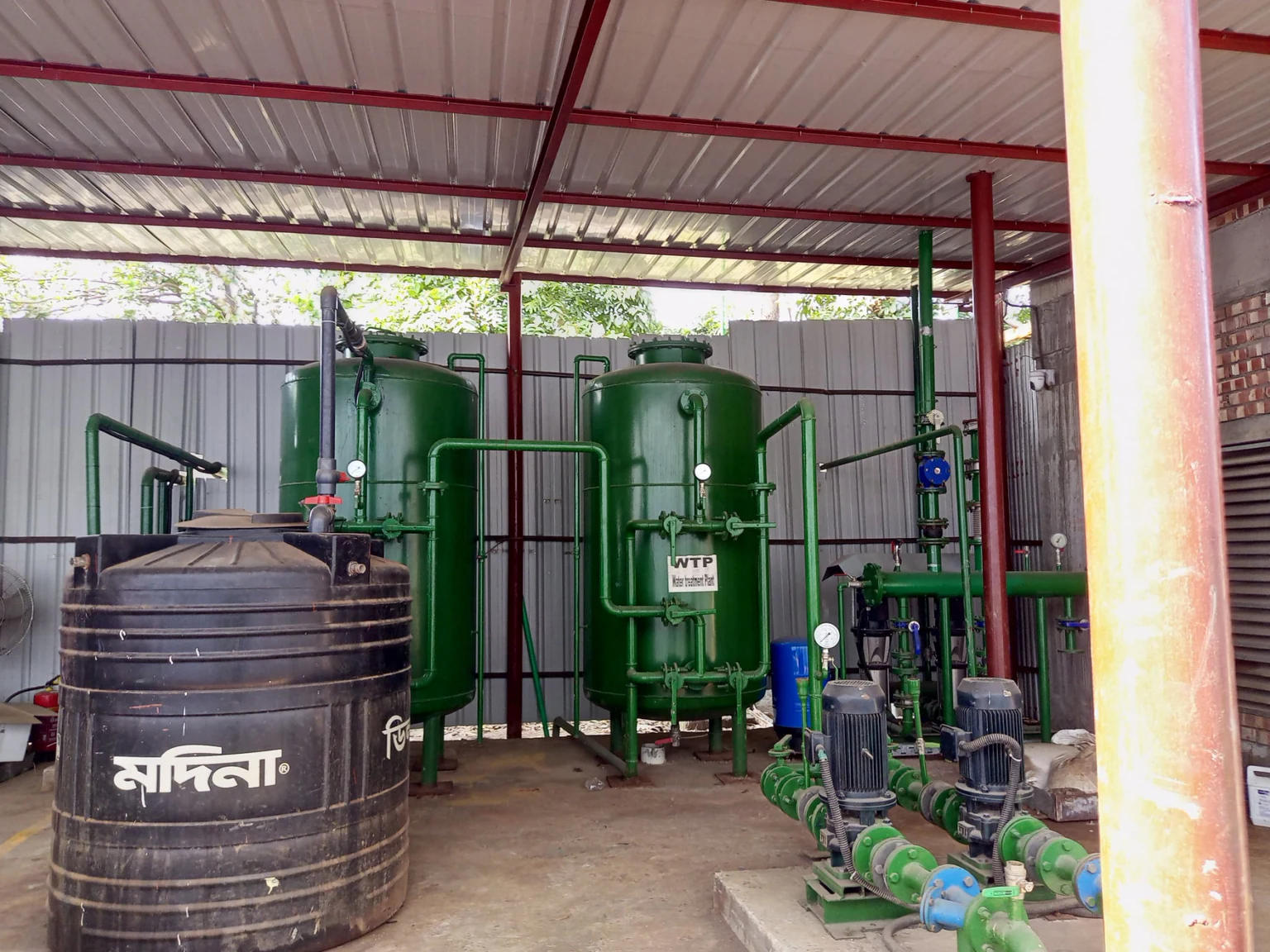 Water treatment plant with green filter vessels, pressure gauges, pumps, pipework and a water storage tank
